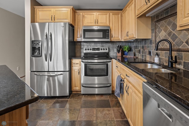 kitchen with appliances with stainless steel finishes, a sink, decorative backsplash, dark stone finish flooring, and dark stone counters