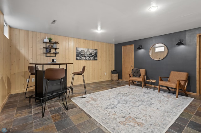sitting room with stone tile flooring, baseboards, and wood walls