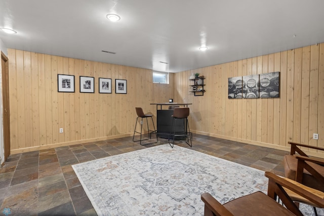 living area featuring stone tile flooring, baseboards, and wood walls
