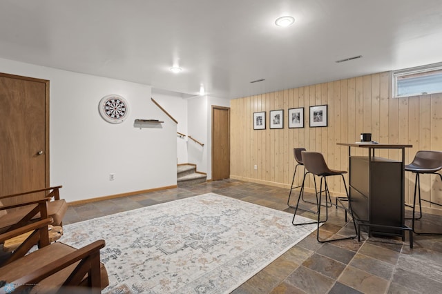 bar area featuring stone tile flooring, baseboards, stairs, and wooden walls