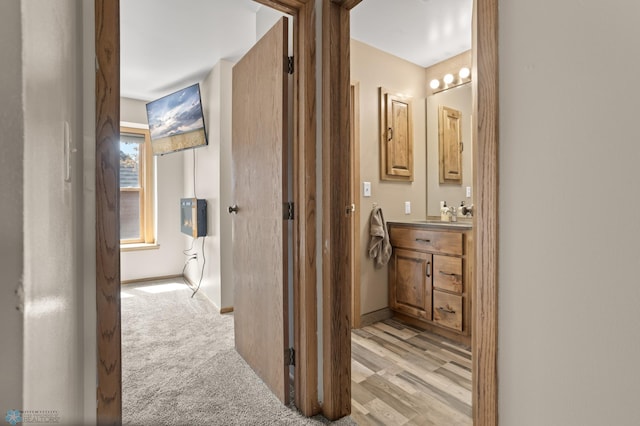 hallway featuring baseboards, light carpet, and a sink