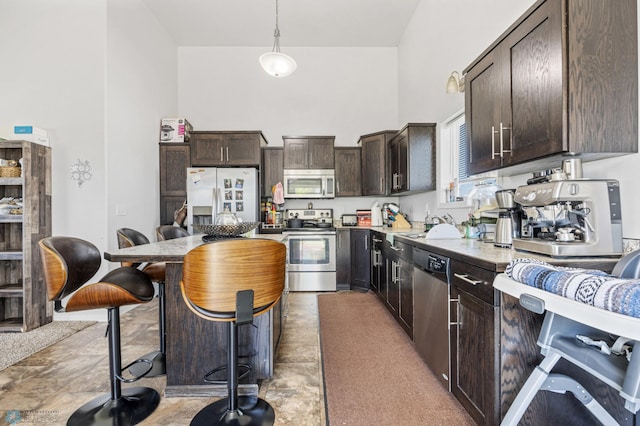 kitchen featuring stainless steel appliances, dark brown cabinetry, a high ceiling, decorative light fixtures, and a sink