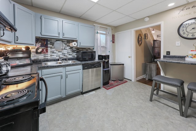 kitchen with dark countertops, a sink, a paneled ceiling, backsplash, and black appliances