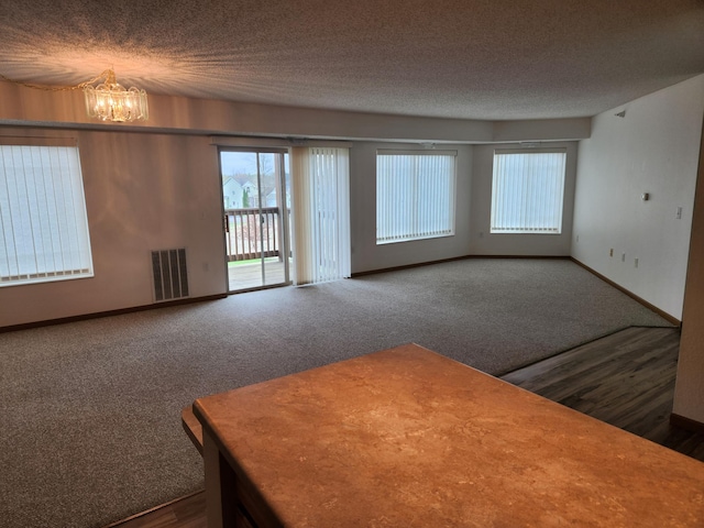 2155 6th Ln SE Unit 212, Cambridge, MN 55008 - unfurnished living room with a chandelier, healthy amount of natural light, a textured ceiling, dark colored carpet, and dark wood finished floors