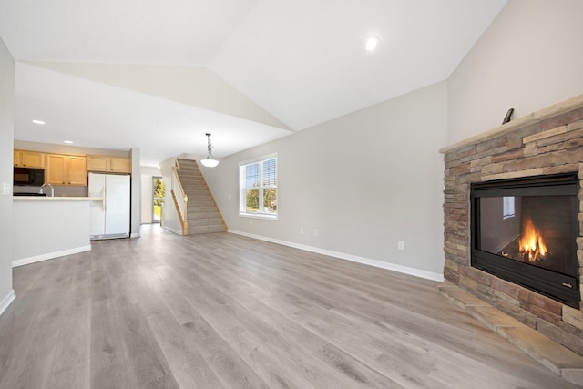 1501 Praha St SE, New Prague, MN 56071 - unfurnished living room featuring light wood-style flooring, baseboards, a stone fireplace, lofted ceiling, and stairs