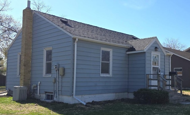 view of home's exterior featuring roof with shingles, a chimney, and cooling unit