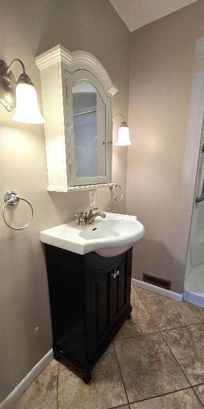 bathroom featuring tile patterned flooring, vanity, baseboards, a shower stall, and visible vents