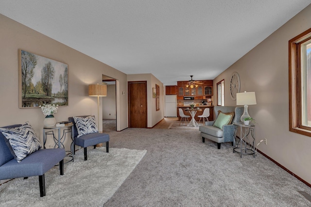 carpeted living area with baseboards and ceiling fan