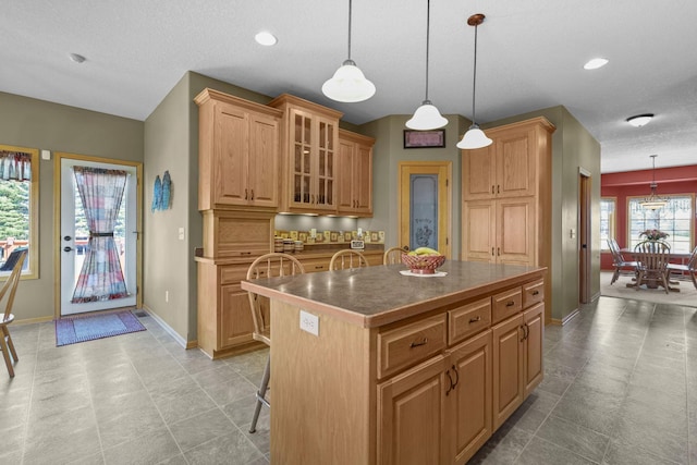 25124 Firefly Ave, Wyoming, MN 55092 - kitchen with baseboards, a center island, glass insert cabinets, pendant lighting, and dark countertops