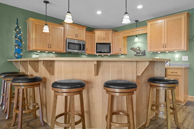 25124 Firefly Ave, Wyoming, MN 55092 - kitchen featuring stainless steel microwave, light brown cabinets, wood finished floors, light countertops, and hanging light fixtures