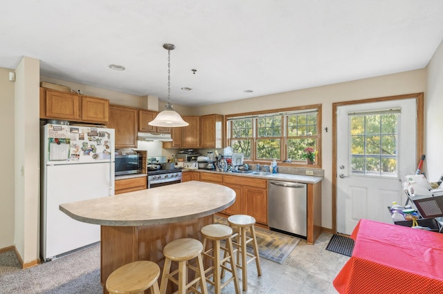 kitchen featuring a center island, light countertops, under cabinet range hood, appliances with stainless steel finishes, and decorative light fixtures