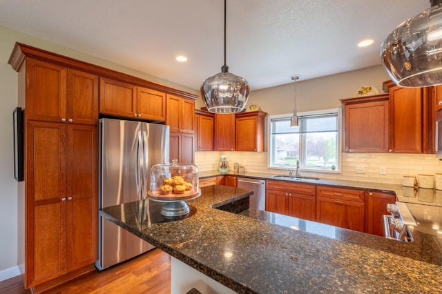 kitchen featuring light wood finished floors, a sink, stainless steel appliances, brown cabinetry, and decorative backsplash