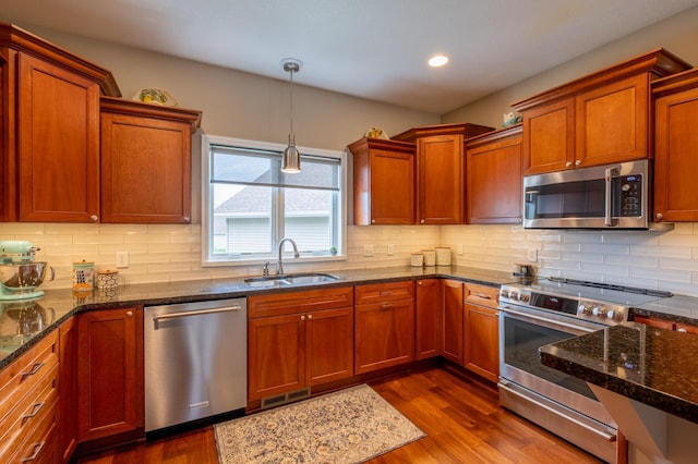 kitchen with a sink, stainless steel appliances, decorative light fixtures, and dark wood-style floors