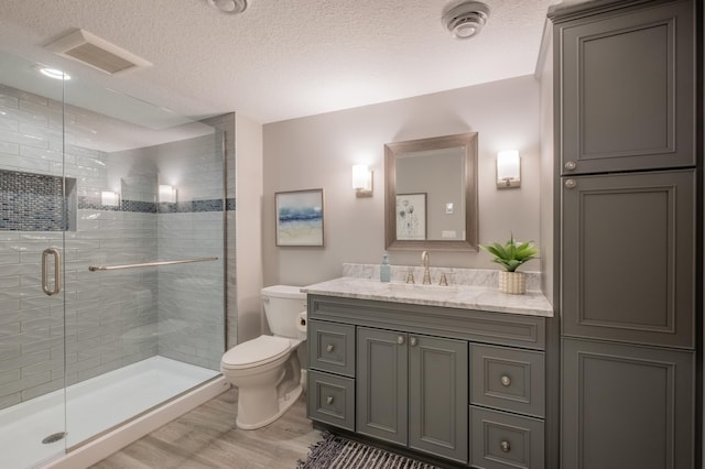 bathroom featuring toilet, vanity, a textured ceiling, visible vents, and a stall shower