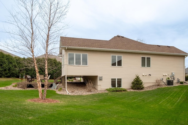 rear view of property featuring central air condition unit, roof with shingles, and a lawn