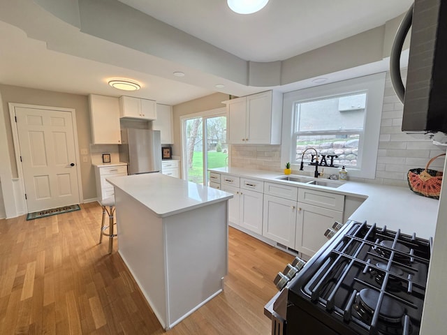kitchen with decorative backsplash, freestanding refrigerator, black range with gas stovetop, a sink, and light wood-style flooring