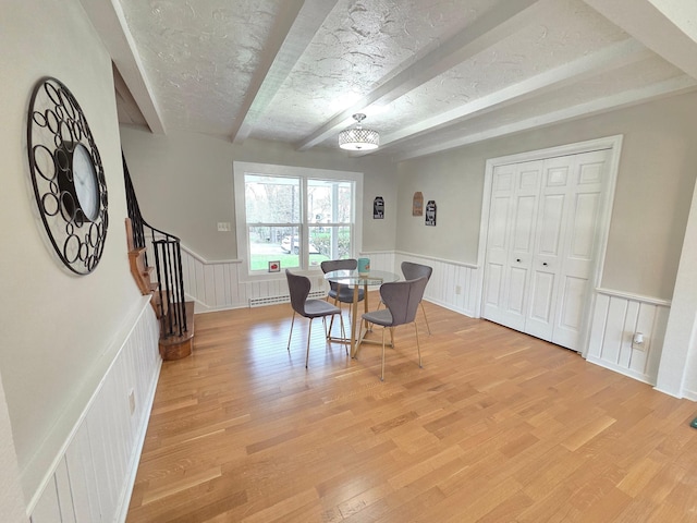 dining area featuring stairs, beamed ceiling, wainscoting, and light wood-style floors