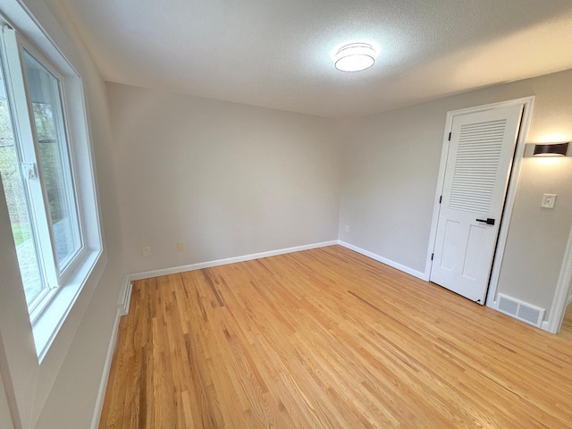 spare room featuring a textured ceiling, baseboards, visible vents, and light wood-style flooring