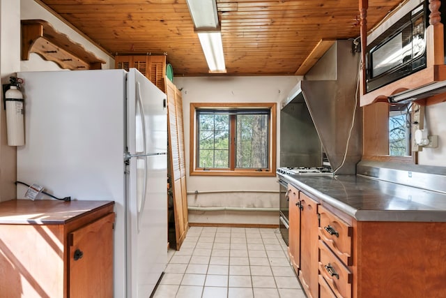 kitchen featuring brown cabinets, freestanding refrigerator, black microwave, light tile patterned floors, and stainless steel counters