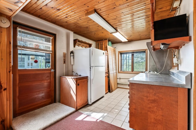 kitchen with light tile patterned floors, brown cabinets, freestanding refrigerator, stainless steel counters, and wooden ceiling