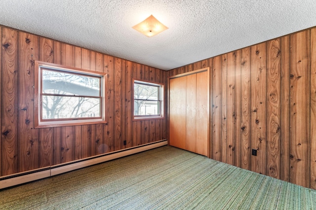 unfurnished room with carpet flooring, a textured ceiling, wood walls, and a baseboard heating unit