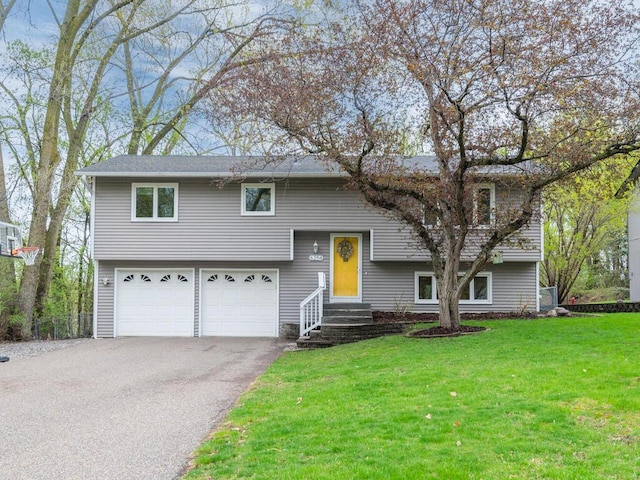 raised ranch featuring an attached garage, driveway, and a front yard