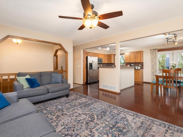 living area featuring visible vents, ceiling fan, dark wood-style floors, and a healthy amount of sunlight