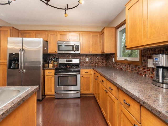 kitchen featuring dark countertops, appliances with stainless steel finishes, a sink, dark wood-type flooring, and backsplash