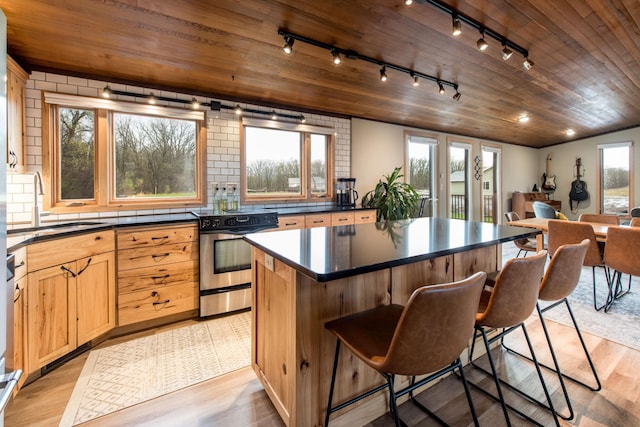 kitchen with track lighting, electric range, dark countertops, a center island, and a sink