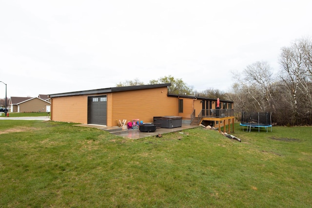 back of house with a garage, a deck, a trampoline, a hot tub, and a yard