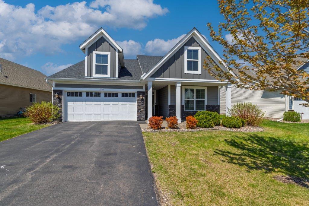 view of front of home with board and batten siding, stone siding, asphalt driveway, and a front lawn