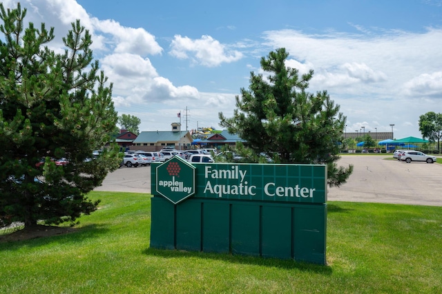 community sign featuring uncovered parking and a lawn