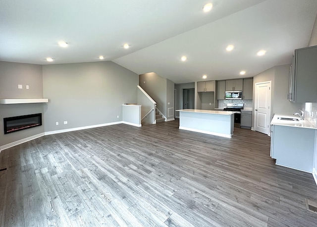 12301 71st Ct NE, Otsego, MN 55330 - unfurnished living room with stairs, baseboards, vaulted ceiling, dark wood-type flooring, and a glass covered fireplace