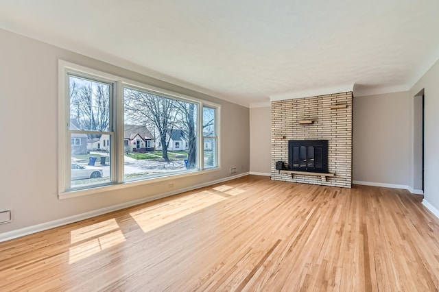 unfurnished living room featuring light wood-style flooring, baseboards, and a brick fireplace