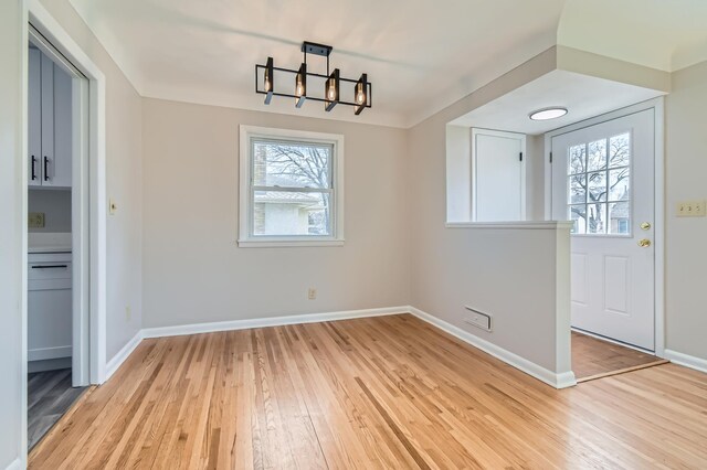 unfurnished dining area with a chandelier, light wood finished floors, and baseboards