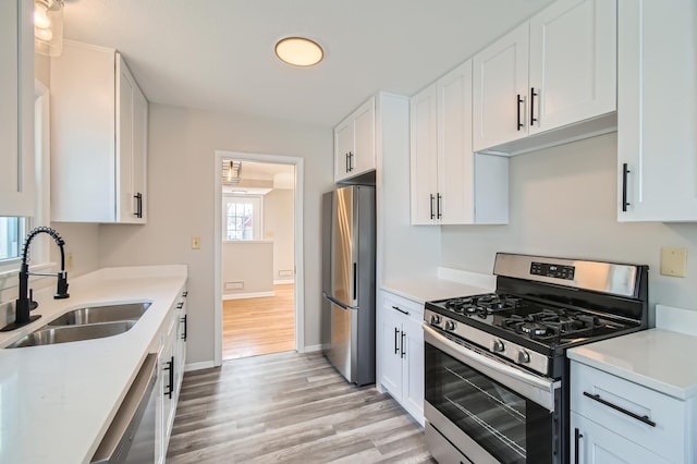 kitchen featuring stainless steel appliances, a sink, light wood-style flooring, white cabinets, and light countertops