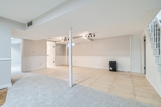 finished below grade area featuring a wainscoted wall, tile patterned flooring, stairway, and carpet