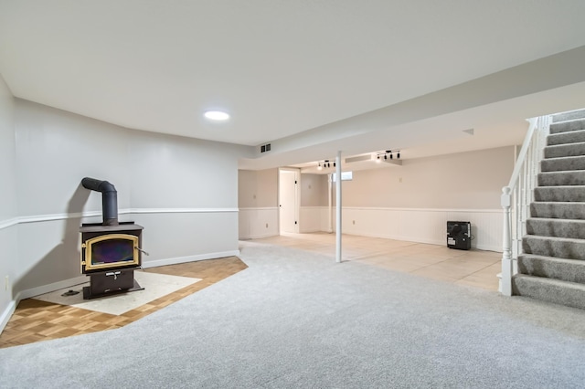finished below grade area featuring stairway, a wood stove, carpet, a wainscoted wall, and baseboards
