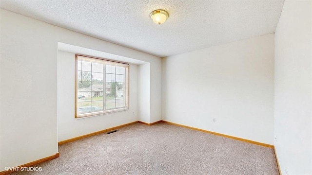 carpeted spare room featuring visible vents, a textured ceiling, and baseboards