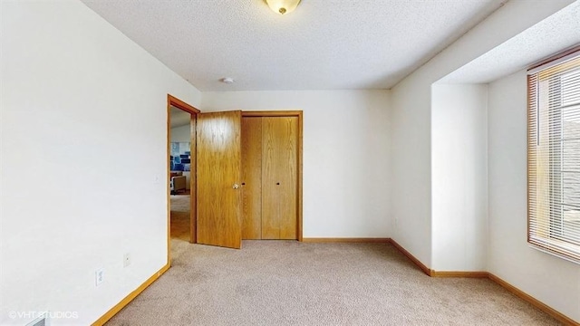 unfurnished bedroom featuring light colored carpet, a textured ceiling, baseboards, and a closet
