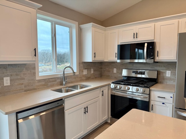 kitchen with a sink, appliances with stainless steel finishes, vaulted ceiling, and light countertops