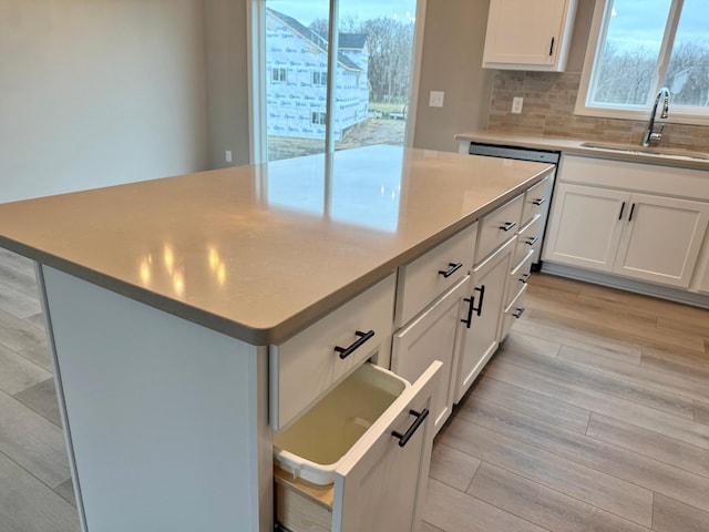 kitchen featuring decorative backsplash, a kitchen island, light wood-style floors, white cabinetry, and a sink
