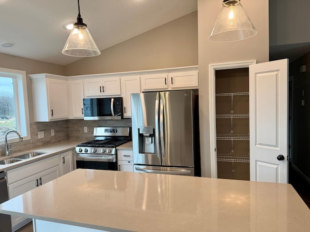 kitchen with appliances with stainless steel finishes, a sink, white cabinetry, decorative backsplash, and vaulted ceiling