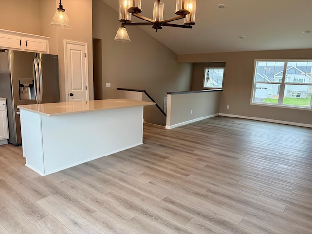 kitchen with a notable chandelier, stainless steel fridge with ice dispenser, light wood-style floors, white cabinetry, and vaulted ceiling