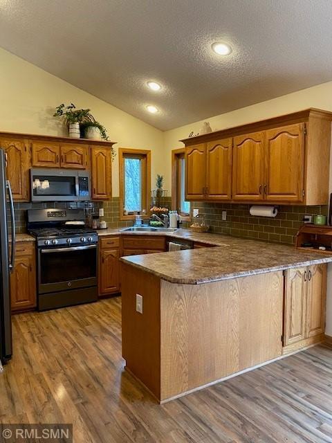 kitchen with a textured ceiling, appliances with stainless steel finishes, a sink, a peninsula, and lofted ceiling