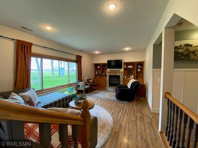 living area featuring a fireplace with raised hearth, visible vents, a wainscoted wall, and light wood-style floors