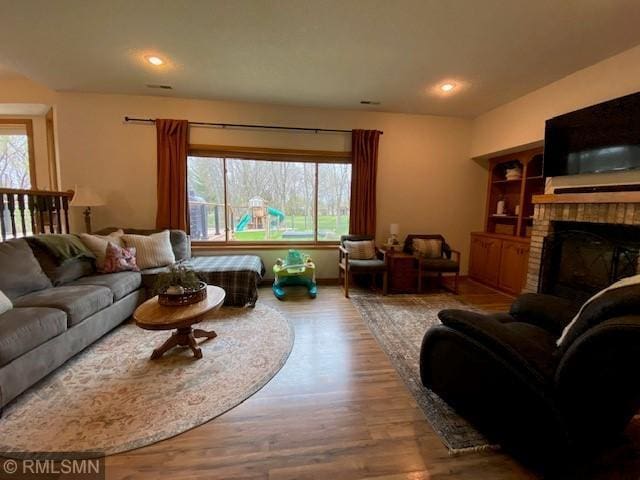 living room with a brick fireplace, wood finished floors, and a healthy amount of sunlight