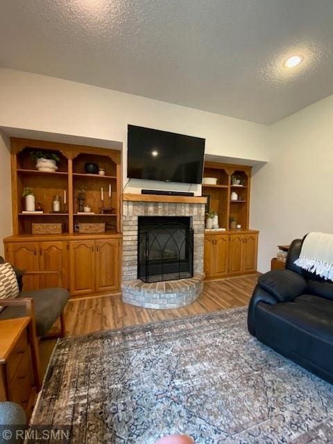 living room featuring a brick fireplace, a textured ceiling, and wood finished floors