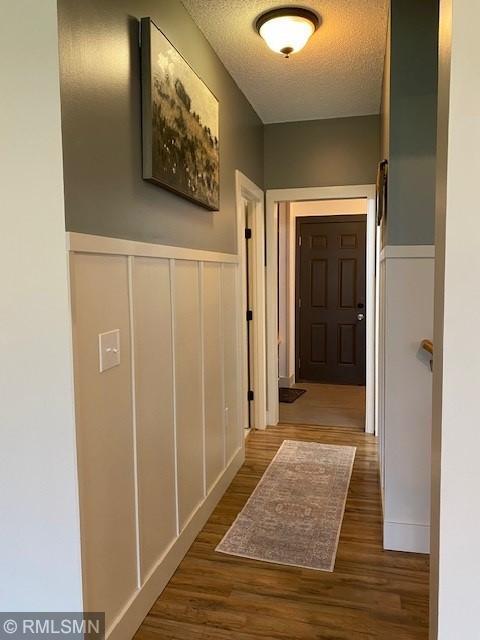 hallway featuring a textured ceiling, wainscoting, wood finished floors, and a decorative wall