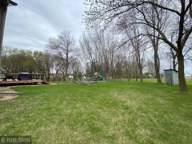 view of yard with a playground, an outbuilding, a deck, and a storage shed